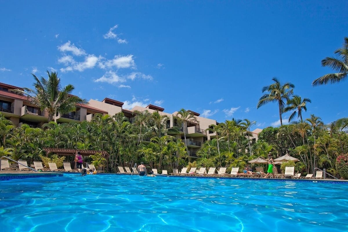 Ein Swimmingpool mit Liegestühlen und Palmen, umgeben von Hotelgebäuden.