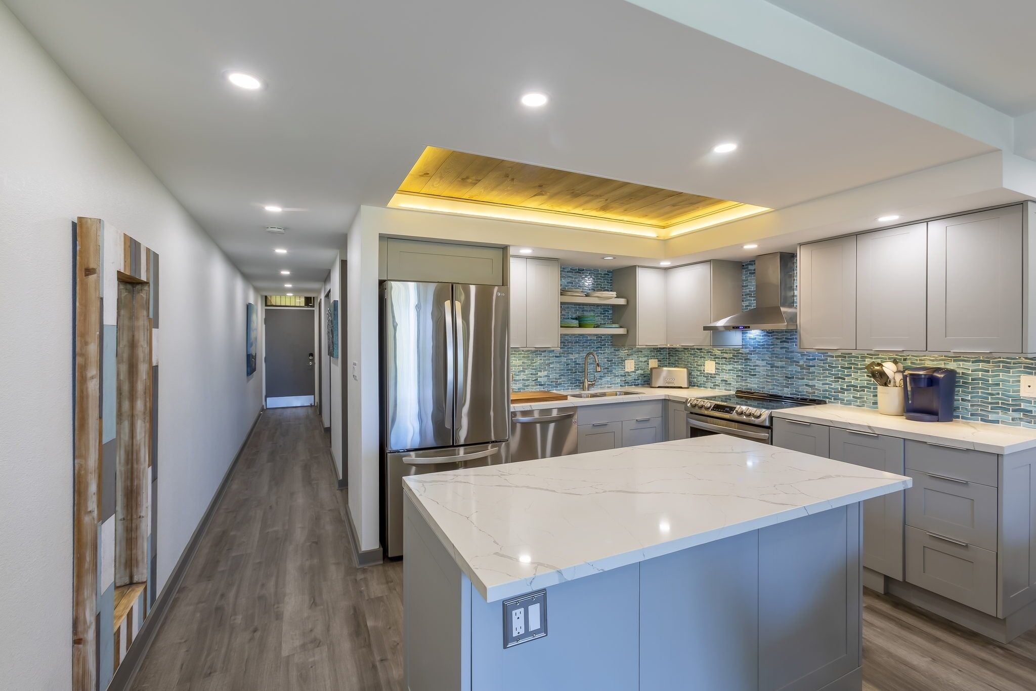 A modern kitchen with a central island, stainless steel appliances, and a blue-tiled backsplash.