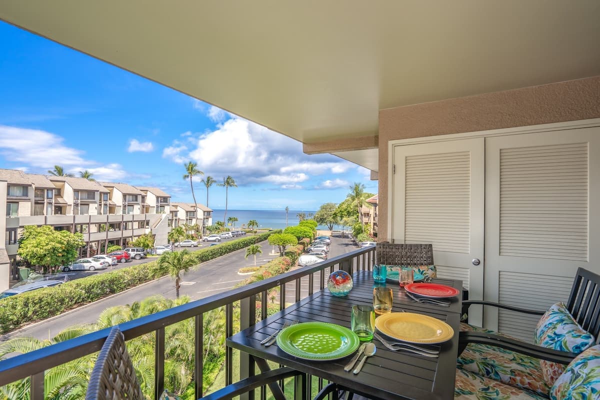 Ein Balkon mit Tisch für zwei Personen, mit Blick auf eine Straße, gesäumt von Palmen, und eine Aussicht auf das Meer.