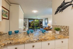 Una cocina con encimera de granito, armarios blancos y un comedor con mesa y sillas.