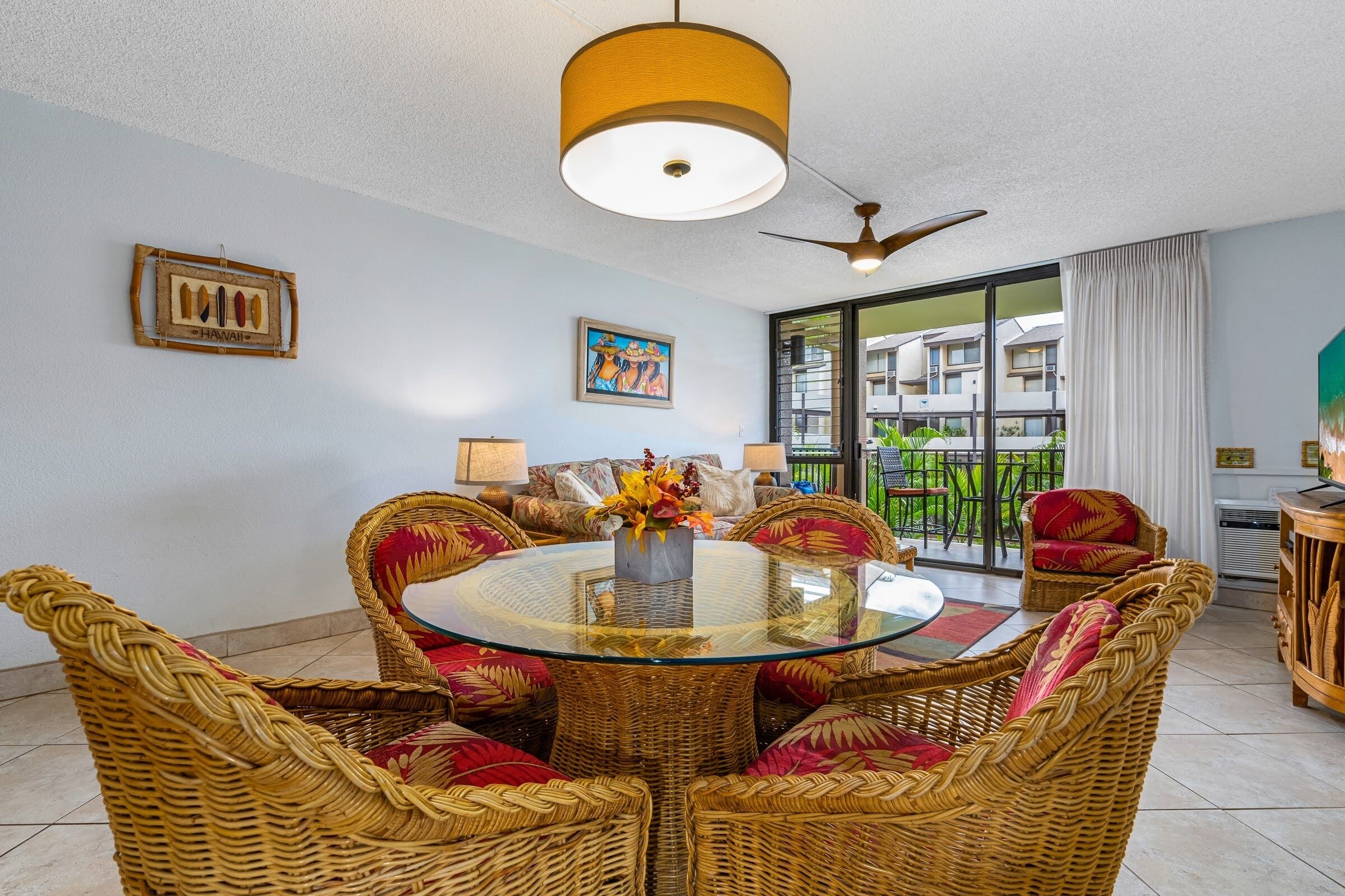 A dining area with wicker furniture, a glass table, and a ceiling fan.