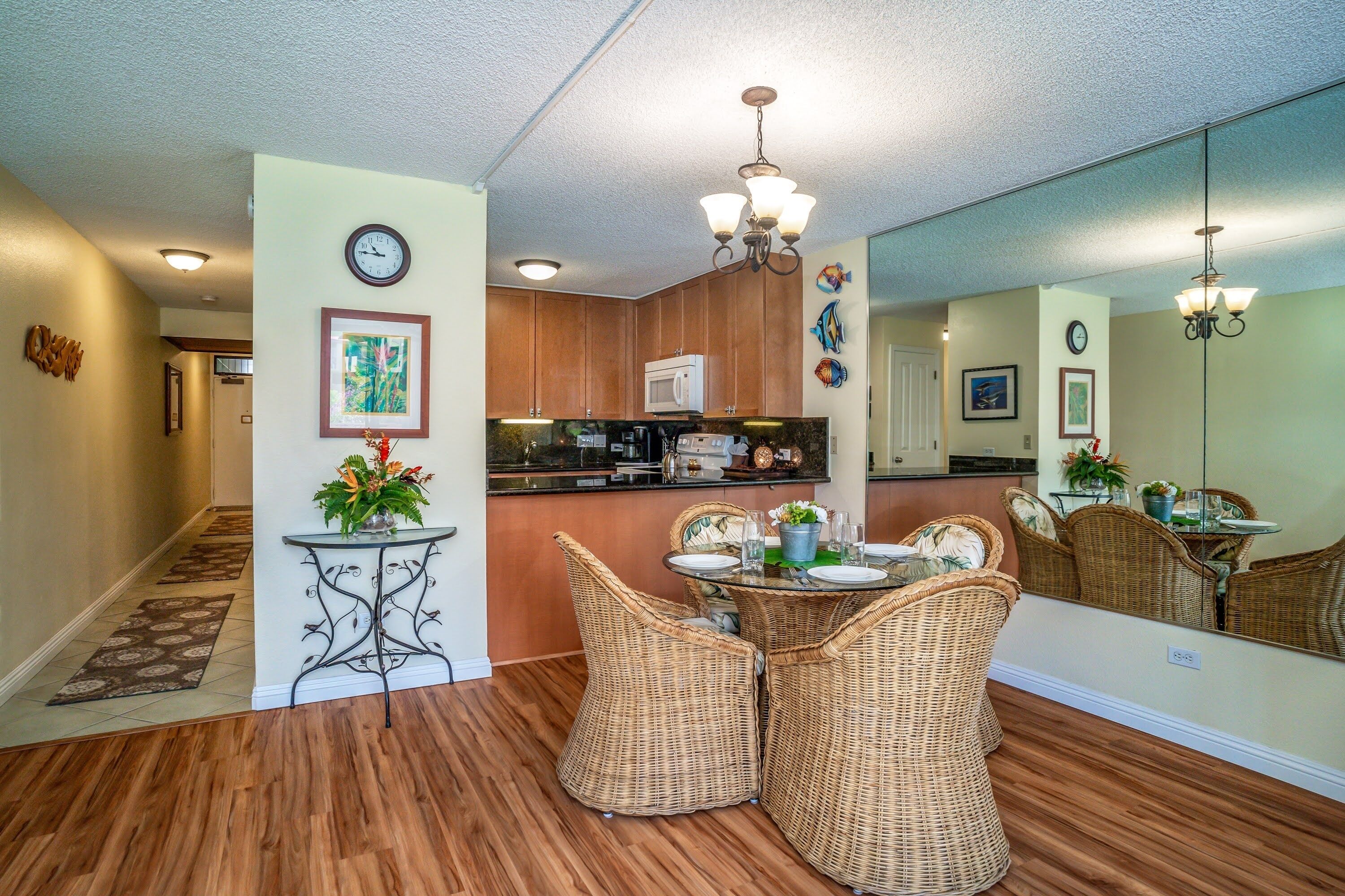 A dining area with wicker chairs, a round table, and a kitchen in the background.