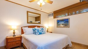 Une chambre d’hôtel comprenant un lit, deux lampes de chevet, un ventilateur de plafond, un grand miroir, un appareil de climatisation, une fenêtre avec vue et un tableau au mur.