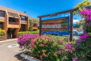 A sign for Kuleana Oceanfront Rentals with a number 3959, surrounded by vibrant purple flowers and a modern building structure.