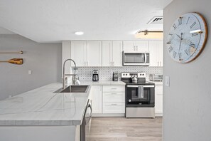 A modern kitchen with white cabinets, stainless steel appliances, and a large wall clock. - Big Island Holualoa Bay Villas by Coldwell Banker Island Vacations (Kailua-Kona)