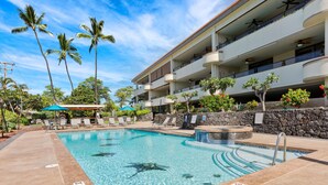 A swimming pool with clear water, surrounded by lounge chairs and palm trees, and a multi-story building with balconies. - Big Island Holualoa Bay Villas by Coldwell Banker Island Vacations (Kailua-Kona)
