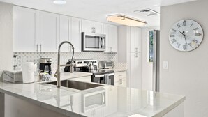 A modern kitchen with white cabinets, stainless steel appliances, and a large island with a sink. - Big Island Holualoa Bay Villas by Coldwell Banker Island Vacations (Kailua-Kona)