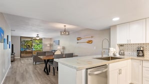 A modern kitchen with white cabinets, a built-in dishwasher, and a dining area with a gray sofa and chairs. - Big Island Holualoa Bay Villas by Coldwell Banker Island Vacations (Kailua-Kona)