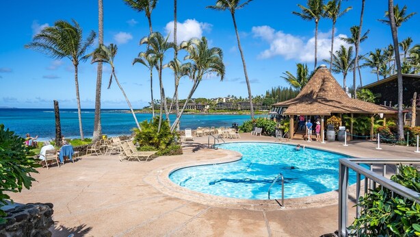 A resort pool area with a curved pool, lounge chairs, and a thatched-roof structure. - Napili Shores by Coldwell Banker Island Vacations (Lahaina)