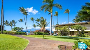 A pathway leading to a building with a 'Beach Access' sign, surrounded by palm trees and a clear blue sky. - Napili Shores by Coldwell Banker Island Vacations (Lahaina)