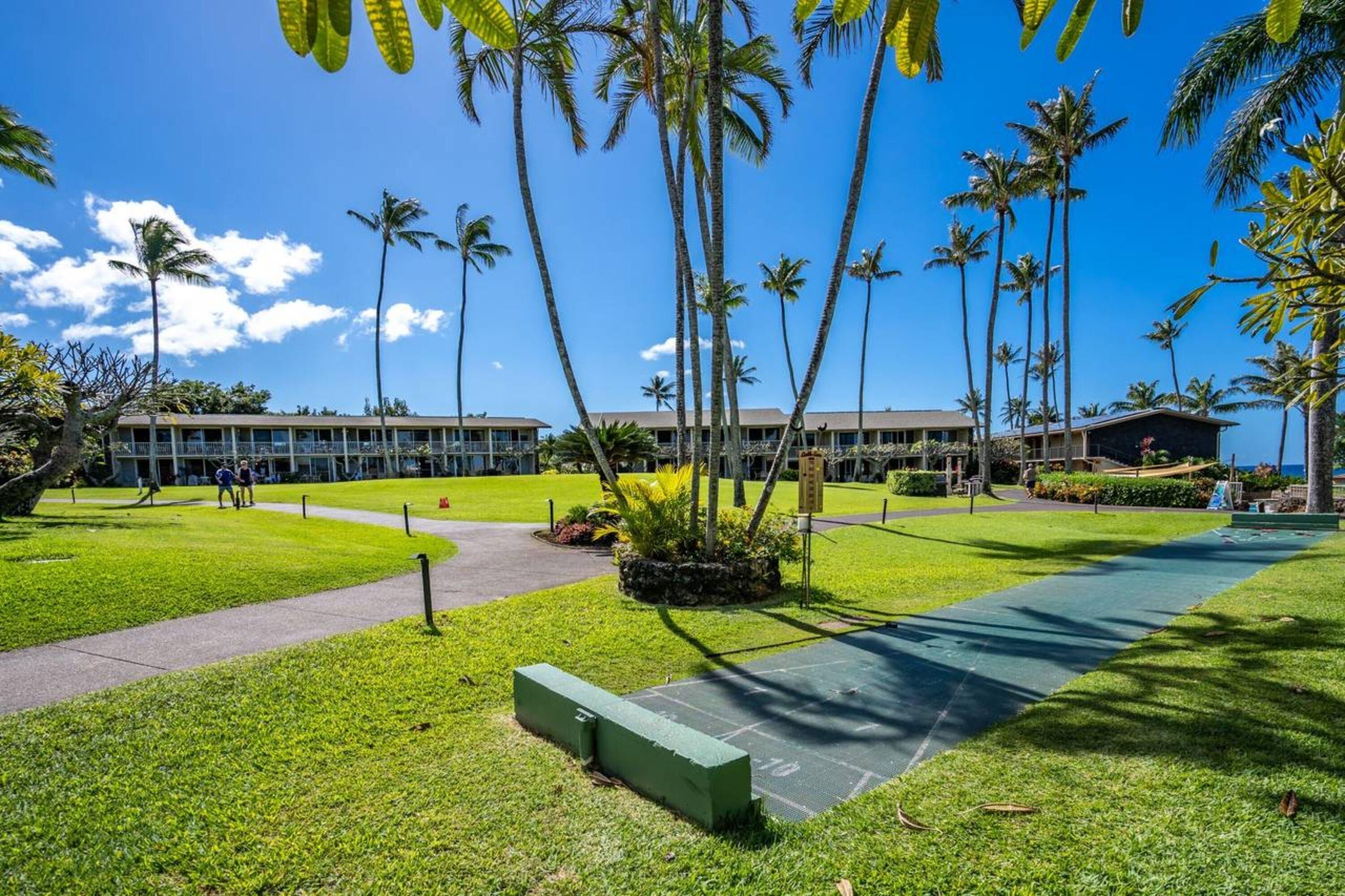 A hotel courtyard with palm trees, a green lawn, and a pathway.