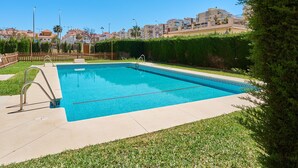 A rectangular swimming pool with a metal ladder, surrounded by a low hedge and a paved deck.