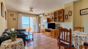 A living room with a sofa, a dining table with chairs, a TV, and a cabinet.