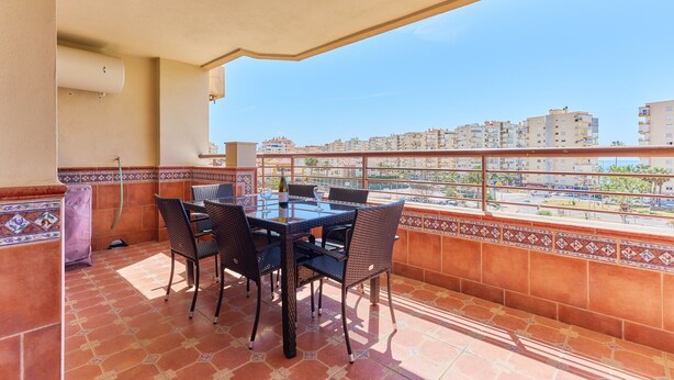 A balcony with a table and chairs, a view of buildings in the distance, and a tiled floor.