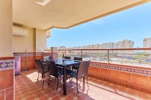 Un balcon avec une table et des chaises, une vue sur des bâtiments au loin et un sol carrelé.