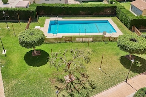 Une piscine rectangulaire entourée d’une clôture en bois, avec une pelouse bien entretenue et quelques arbres.