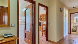 A hallway with wooden doors, a tiled floor, a wooden cabinet, and a small table with a device.