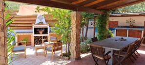 Eine Terrasse im Freien mit einer Steinsäule, Holzstühlen, einem Tisch und einem Grill.