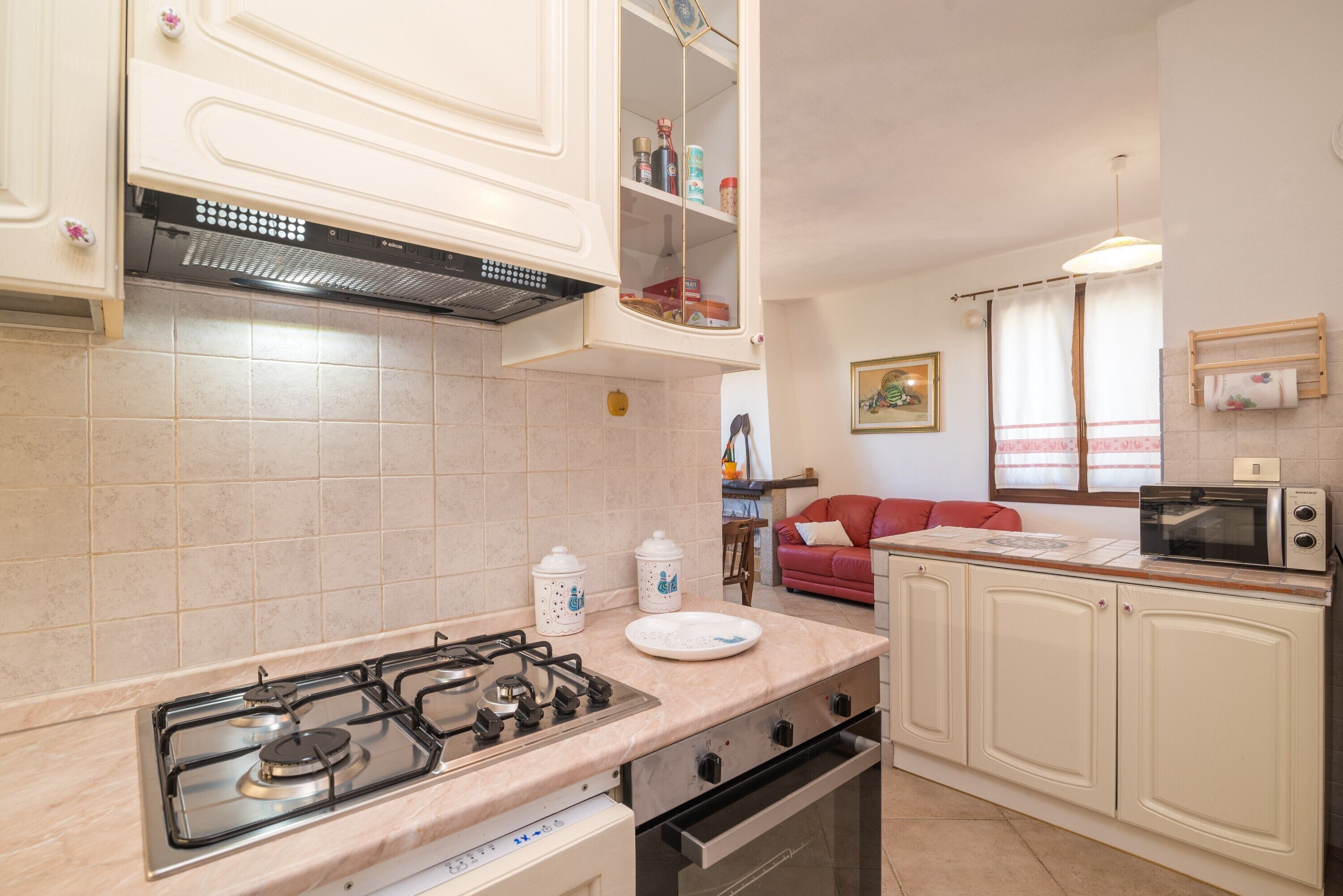 A kitchen with a gas stove, oven, and microwave. There is a red sofa in the background.