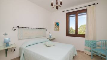 Ein Schlafzimmer mit Bett, Nachttisch, Lampe, Stuhl, Fenster und einer Chandelier.