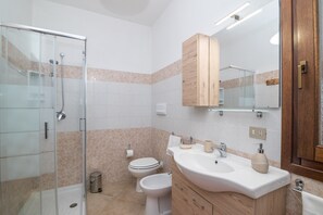 Ein modernes Badezimmer mit Duschkabine aus Glas, Toilette, Bidet, Waschbecken mit Spiegel und Holzschränken.