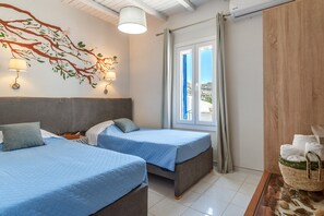 A hotel room with two beds, a wall mural, a window with curtains, and a basket of towels.