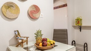 En matplats med ett glasbord, en stol, en fruktskål och dekorativa, vävda tallrikar på väggen.