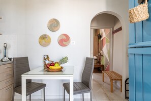 A dining area with a white table, two chairs, a fruit bowl, and decorative plates on the wall.