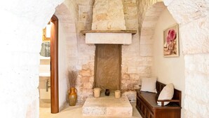 Una habitación de paredes de piedra con chimenea, un banco de madera y un cuadro en la pared.