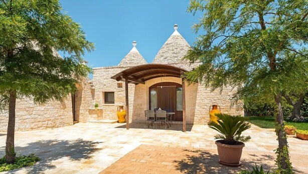Un edificio de piedra con un patio cubierto, una mesa y sillas, y plantas en macetas.