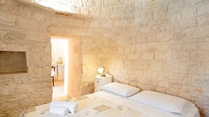Habitación con paredes de piedra, una cama, una mesita de noche y una lámpara.