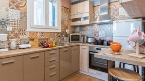 A kitchen with a microwave, oven, and various appliances. There are wooden cabinets and a window above the sink. - Holiday Home 'Porto Galini Tinos Perastra 103' with Sea View, Wi-Fi and Air Conditioning (?a??t?)
