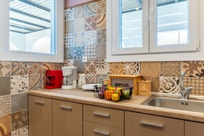 Une cuisine avec des carreaux décoratifs, une machine à café, un panier de fruits et une boîte à pain.