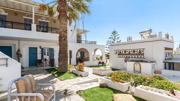 A courtyard with a palm tree, outdoor seating, and a building with a white facade and blue doors. - Holiday Home 'Porto Galini Tinos Perastra 103' with Sea View, Wi-Fi and Air Conditioning (?a??t?)