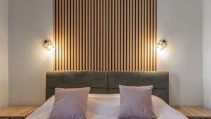 Un lit avec une tête de lit grise, deux tables de chevet et des lampes fixées au mur.