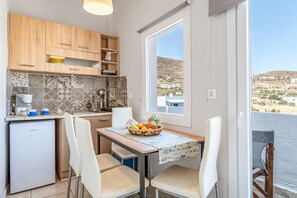 A compact kitchen with a dining area, a small refrigerator, and a window with a view of a hilly landscape.