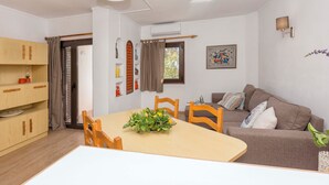Una sala moderna con una mesa de comedor, sillas de madera, un sofá y una planta decorativa en el centro.