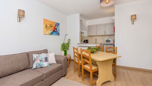 Una sala de estar moderna con un sofá, una mesa de comedor y sillas. Se ve una cocina al fondo con armarios y electrodomésticos.