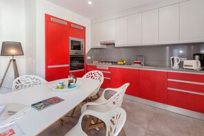 A modern kitchen with red cabinetry, a white dining table, and a white chair. - Villa 'Petala' with Private Pool, Wi-Fi and Air Conditioning (Albufeira)