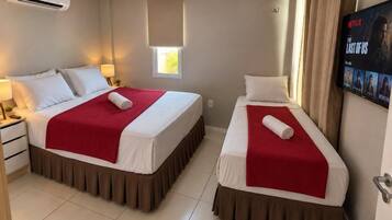 A hotel room with two beds, a TV, and an air conditioning unit.