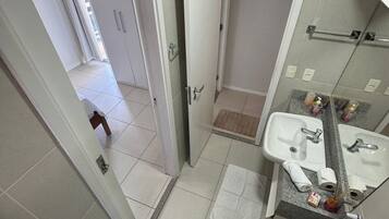 A bathroom with a toilet, sink, and mirror. There is a towel on the floor and toiletries on the sink.