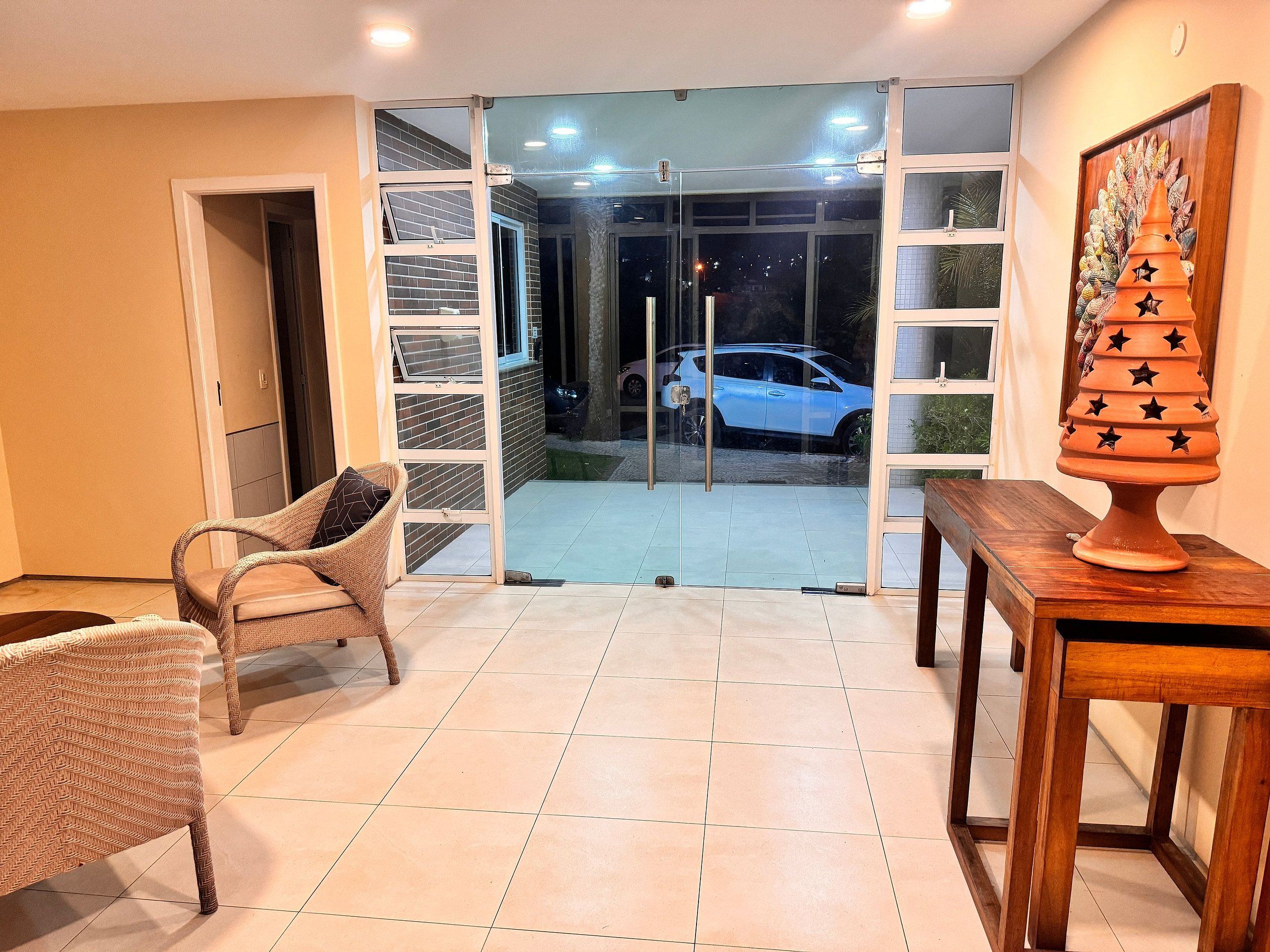 A room with a sliding glass door leading to a balcony, a wicker chair, a wooden table, and a decorative pot.