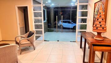 A room with a sliding glass door leading to a balcony, a wicker chair, a wooden table, and a decorative pot.