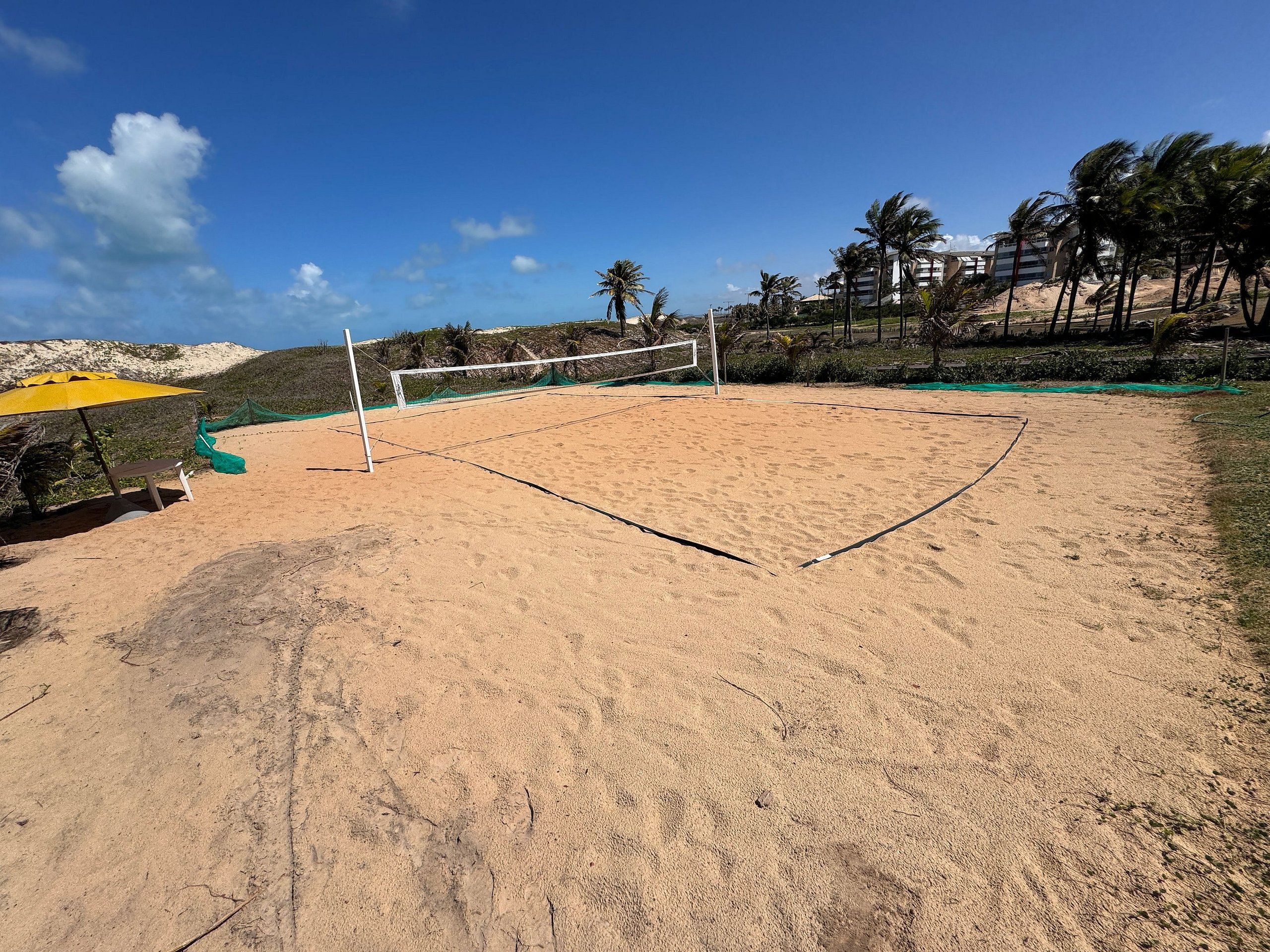 A sandy beach volleyball court with a net, a bench, and a yellow umbrella.