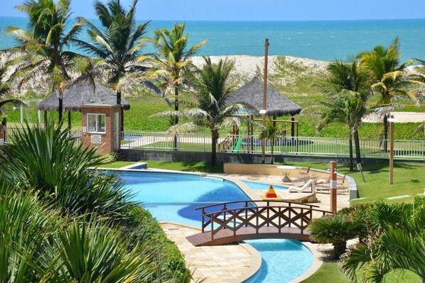 A pool area with a bridge, palm trees, and a beach view. - GranSol, Terreo, Pé na areia, 03 qtos, Até 10 hóspedes, vizinho ao B.PARK (Aquiraz)