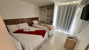 A hotel room with two beds, a TV, a shelf with towels, and a window with curtains. - GranSol, Terreo, Pé na areia, 03 qtos, 08 hóspedes, a 600m do B PARK (Aquiraz)