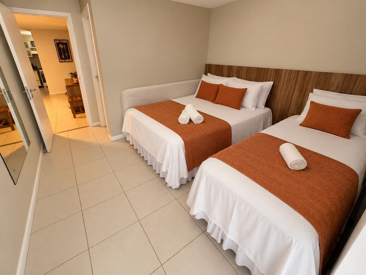 Habitación de hotel con dos camas, cada una con cubrecama blanco y almohadas naranjas, y cabecero de madera.