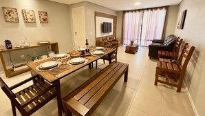 A dining area with a wooden table set for four, a sofa, and a TV mounted on the wall. - GranSol, Terreo, Pé na areia, 03 qtos, 08 hóspedes, a 600m do B PARK (Aquiraz)