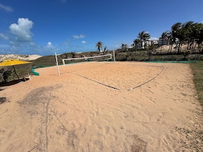 A sandy beach volleyball court with a net, a bench, and a yellow umbrella. - GranSol, Terreo, Pé na areia, 03 qtos, Até 10 hóspedes, vizinho ao B.PARK (Aquiraz)
