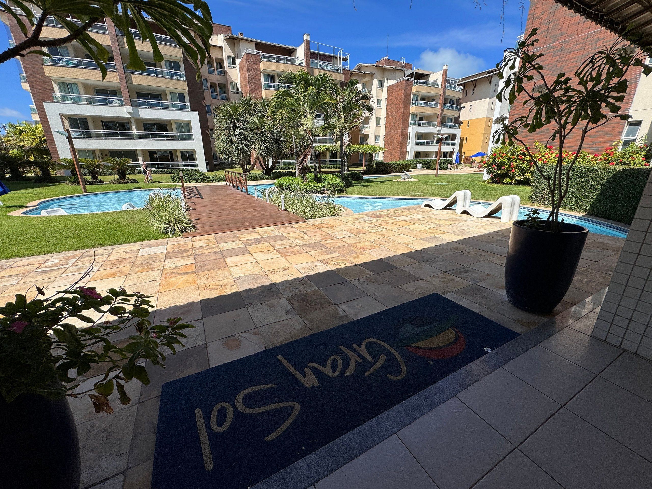 Un conjunto residencial con piscina, terraza de madera y zona pavimentada con colchoneta para juegos infantiles.